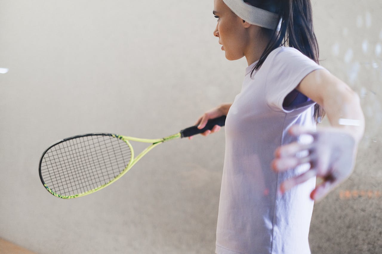 A woman playing tennis indoors, focusing on her swing with a tennis racket.