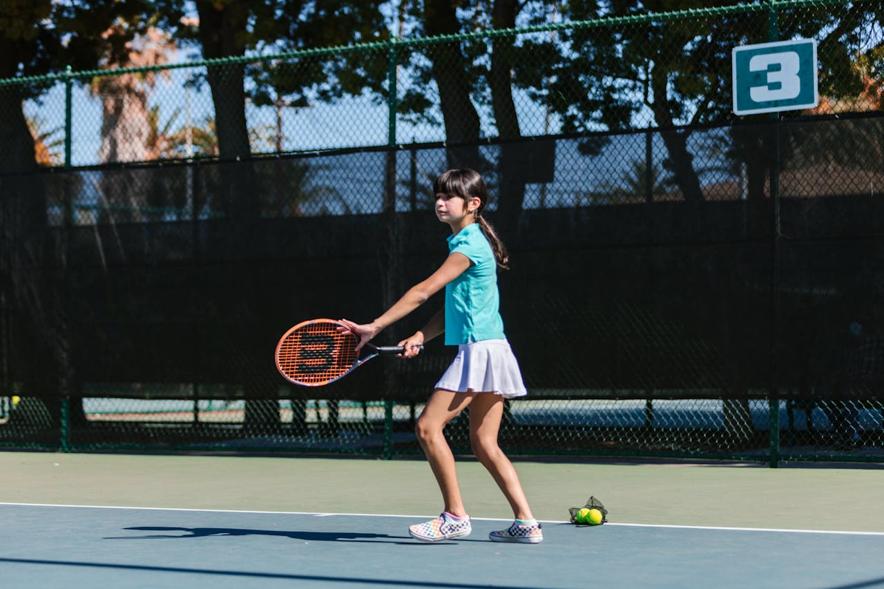 Young girl in sportswear practicing tennis outdoors during the day.