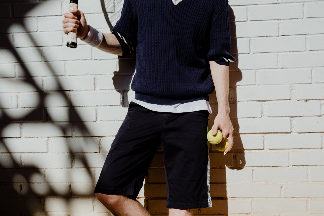 Caucasian tennis player stands by a white brick wall with racket and tennis ball.